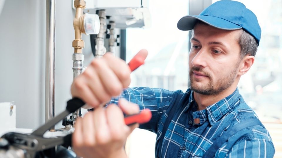 contractor in a blue shirt and hat fixing pipes